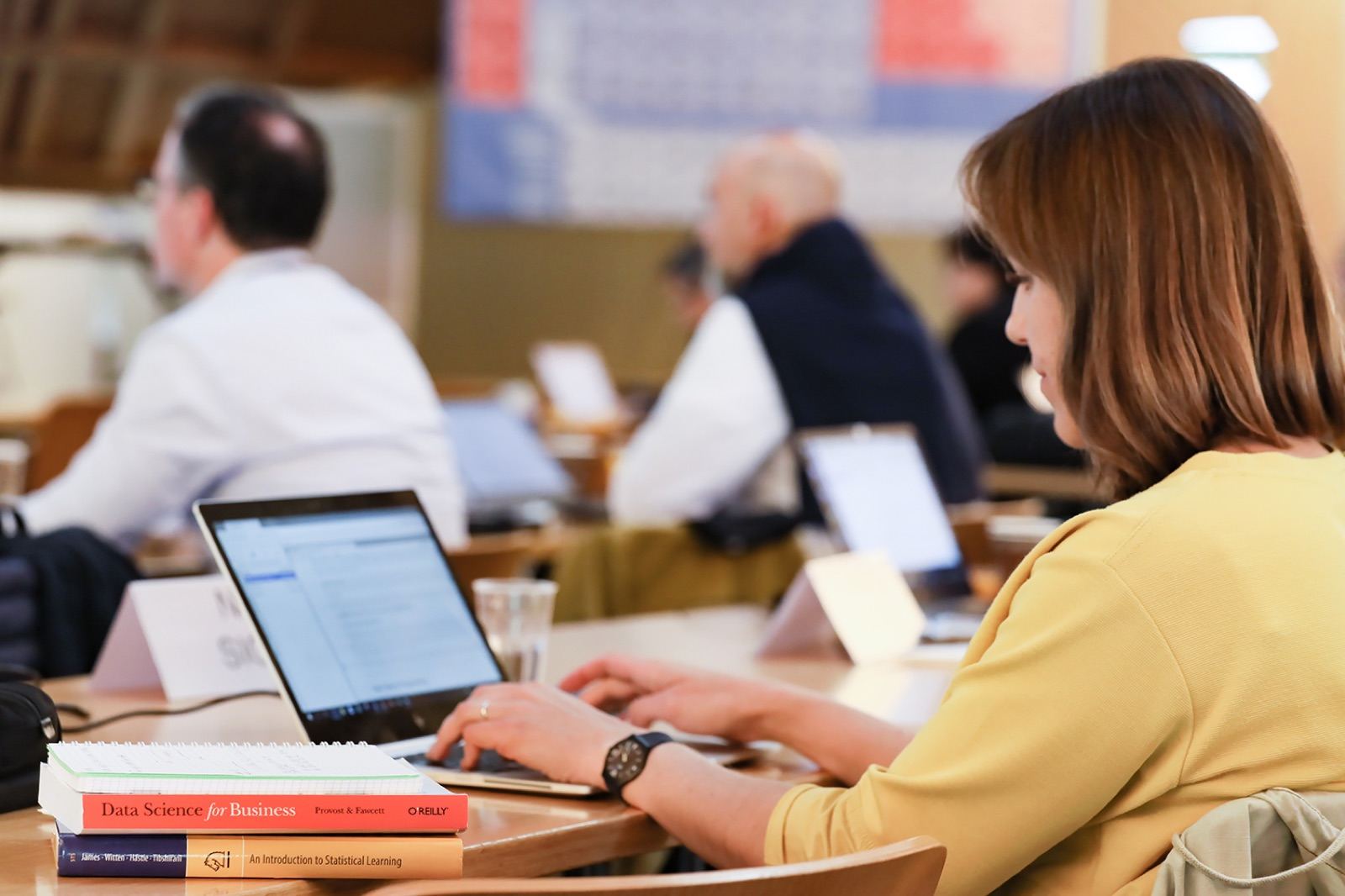Participants working on laptops during the Data Science for Managers program, with data-science textbooks on the desk