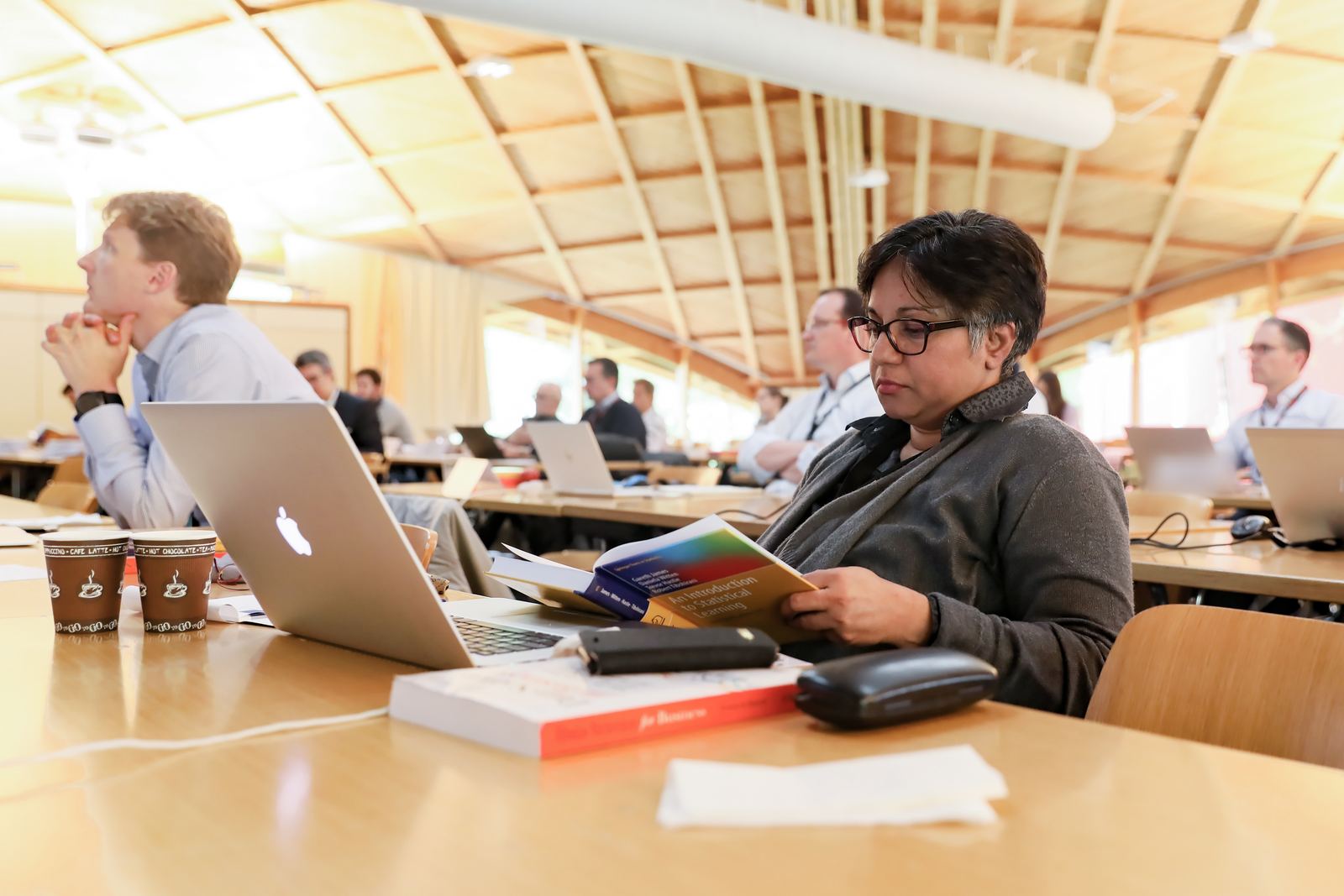 An executive-program participant reads a statistics textbook at her desk while others follow the lecture