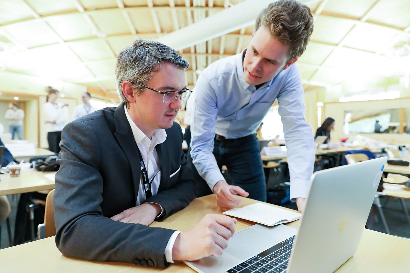 A teaching assistant leans over to help a participant working through an exercise on a laptop